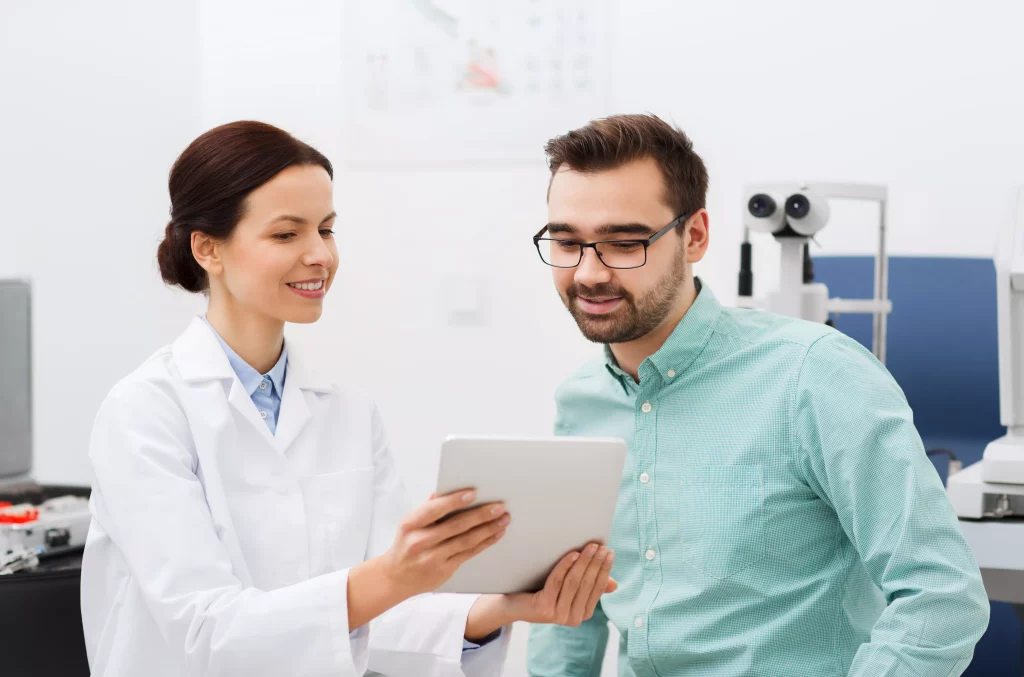 Ärztin zeigt auf Tablet, Patient im Behandlungsraum